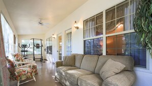 Ein geräumiges Wohnzimmer mit einem beigen Sofa, einem blumigen Sessel und einem Deckenventilator.