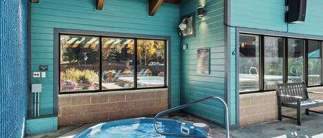 A hot tub with a wooden deck, a bench, and a window overlooking a garden.