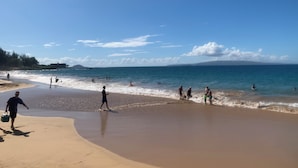 Ein Strand mit Menschen, die spazieren gehen und schwimmen, klarem Himmel und ruhiger See.