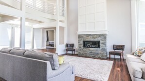 A spacious living room with a stone fireplace, a grey sofa, and a white armchair. - King Of The Mountain, Panoramic View, allows UP TO 40 Guests Completely Seclude (Laketown)