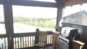 A covered outdoor area with a grill, wooden deck, and a view of the landscape. - Large cozy modern cabin  (Centennial)