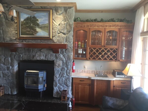 A stone fireplace with a wood-burning stove, wooden cabinets with glass doors, and a painting above the fireplace.