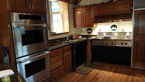 A kitchen with wooden cabinets, stainless steel appliances, a window, and a decorative plate on the wall. - Large cozy modern cabin  (Centennial)