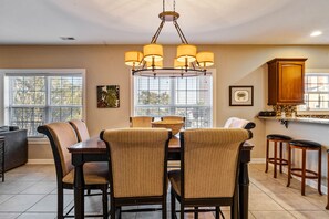 A dining area with a chandelier, wicker chairs, a table, and a kitchen area with stools and a cabinet. - Grand Ocean Getaway III, Private Pool ! (North Myrtle Beach)