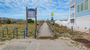 A wooden boardwalk leading to a beach area with a sign indicating 'CLAM SHELL' and beach rules.