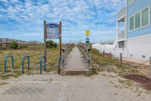 Une promenade en bois mène à une zone de plage où un panneau indique « CLAM SHELL » et rappelle les règles à respecter sur la plage.