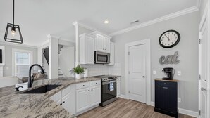 A modern kitchen with white cabinetry, a stainless steel microwave, a built-in oven, and a coffee maker on a wooden cabinet.