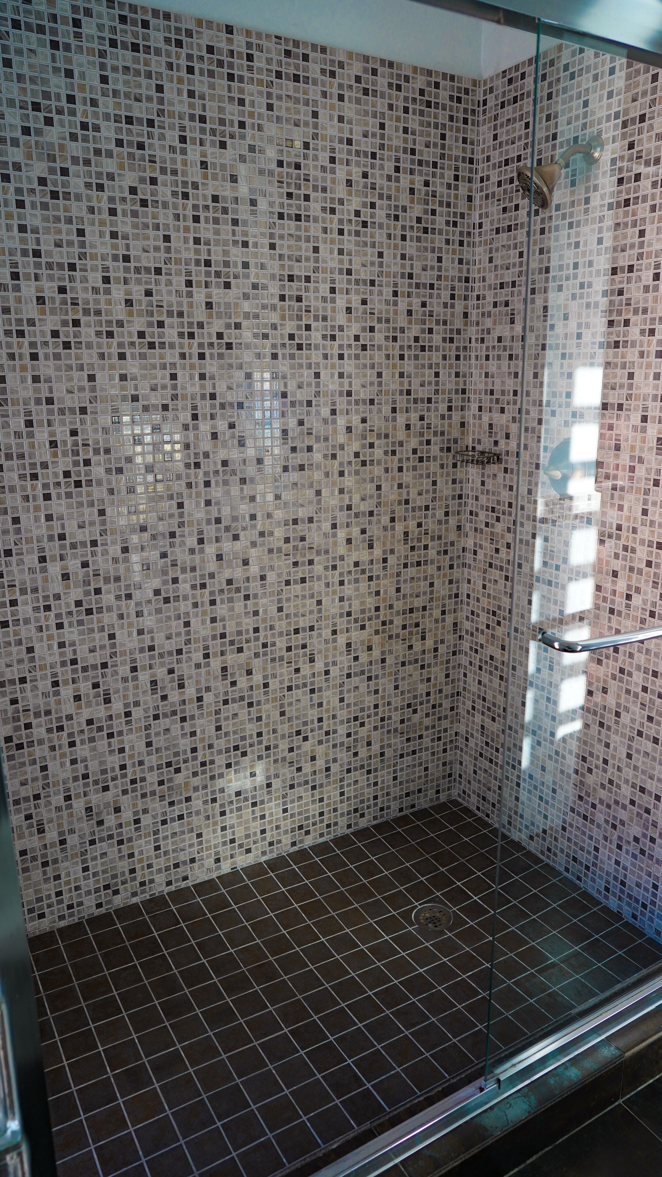 A shower with mosaic tile walls and a tiled floor.