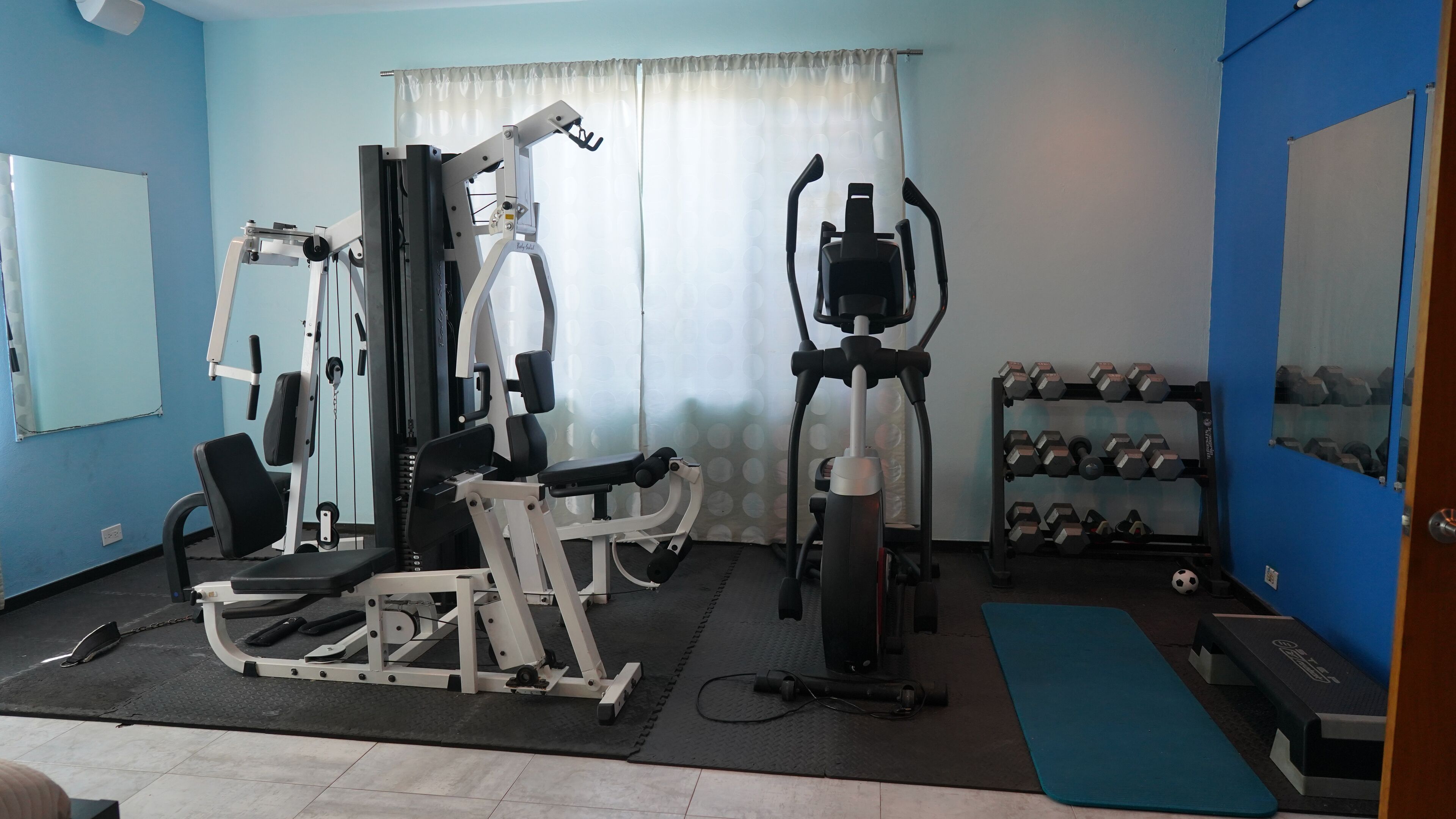 A gym with exercise equipment, a dumbbell rack, and a blue mat.