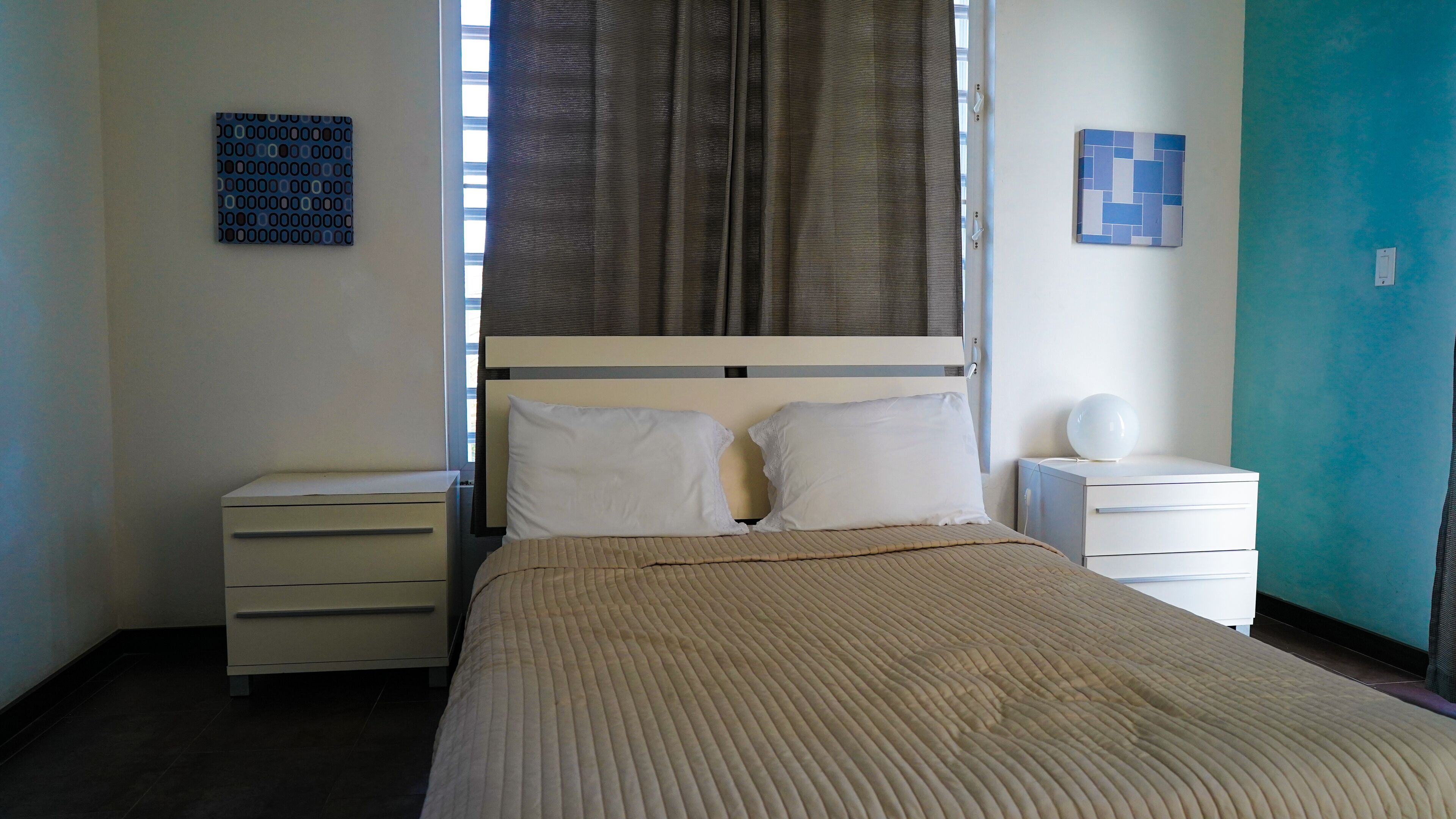 Una camera da letto ordinata con un letto, due comodini, un tavolino, una lampada a parete e una finestra con tende.