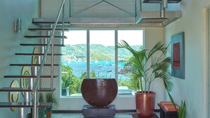 Un interior espaiós amb una escala moderna, grans finestres que donen vista al mar i una bressol decoratiu al centre.