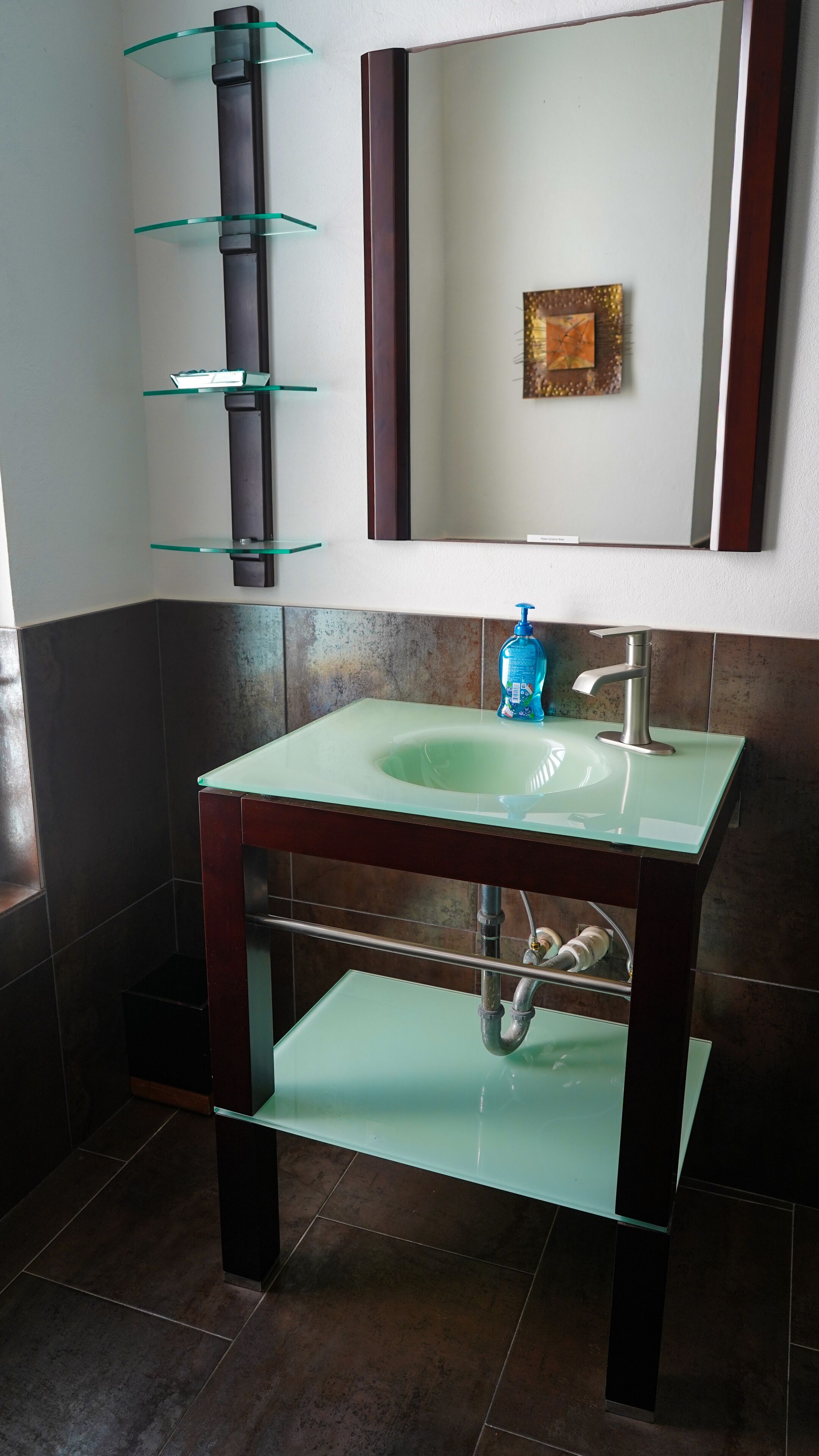 A bathroom with a glass sink, a mirror, and a soap dispenser.