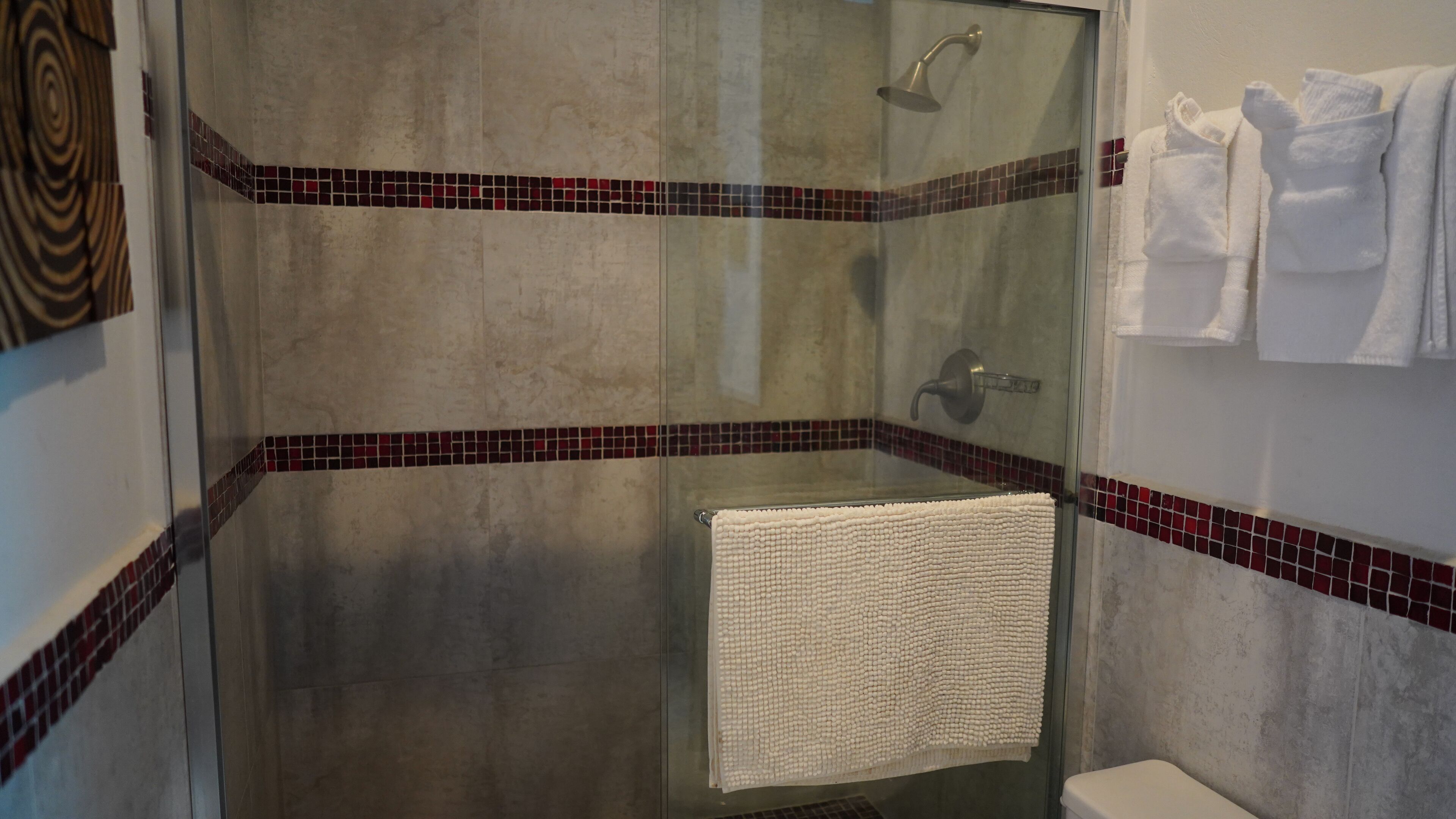 A glass-enclosed shower with a tiled floor and walls, a white towel hanging on a rack, and a white toilet.