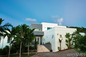 A modern two-story house with a white exterior, a staircase leading to the entrance, and a well-maintained garden with palm trees. - Contemporary  Waterfront Luxury Estate Views,Pool,AC,Gym (St. Thomas)
