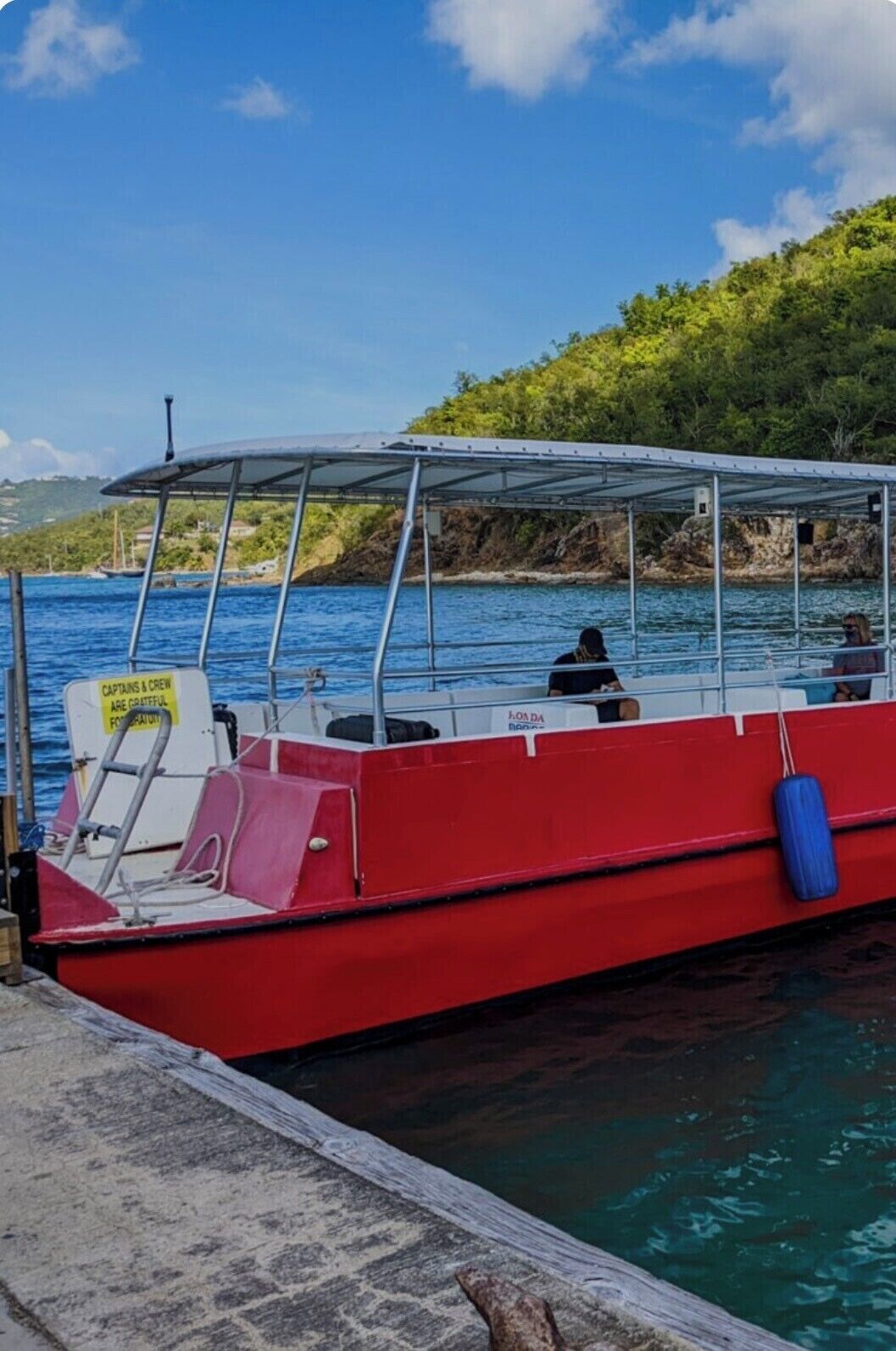 A red boat docked at a pier with a covered seating area and a sign indicating crew gratitude.