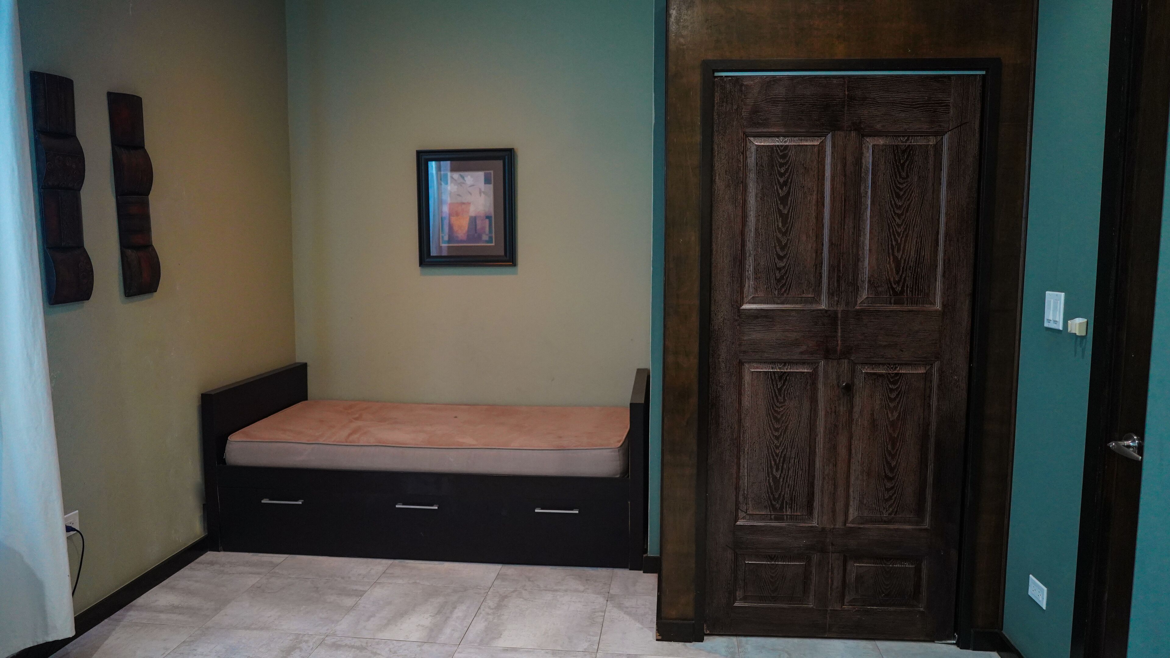 Une pièce avec un lit, une porte et un tableau accroché au mur.