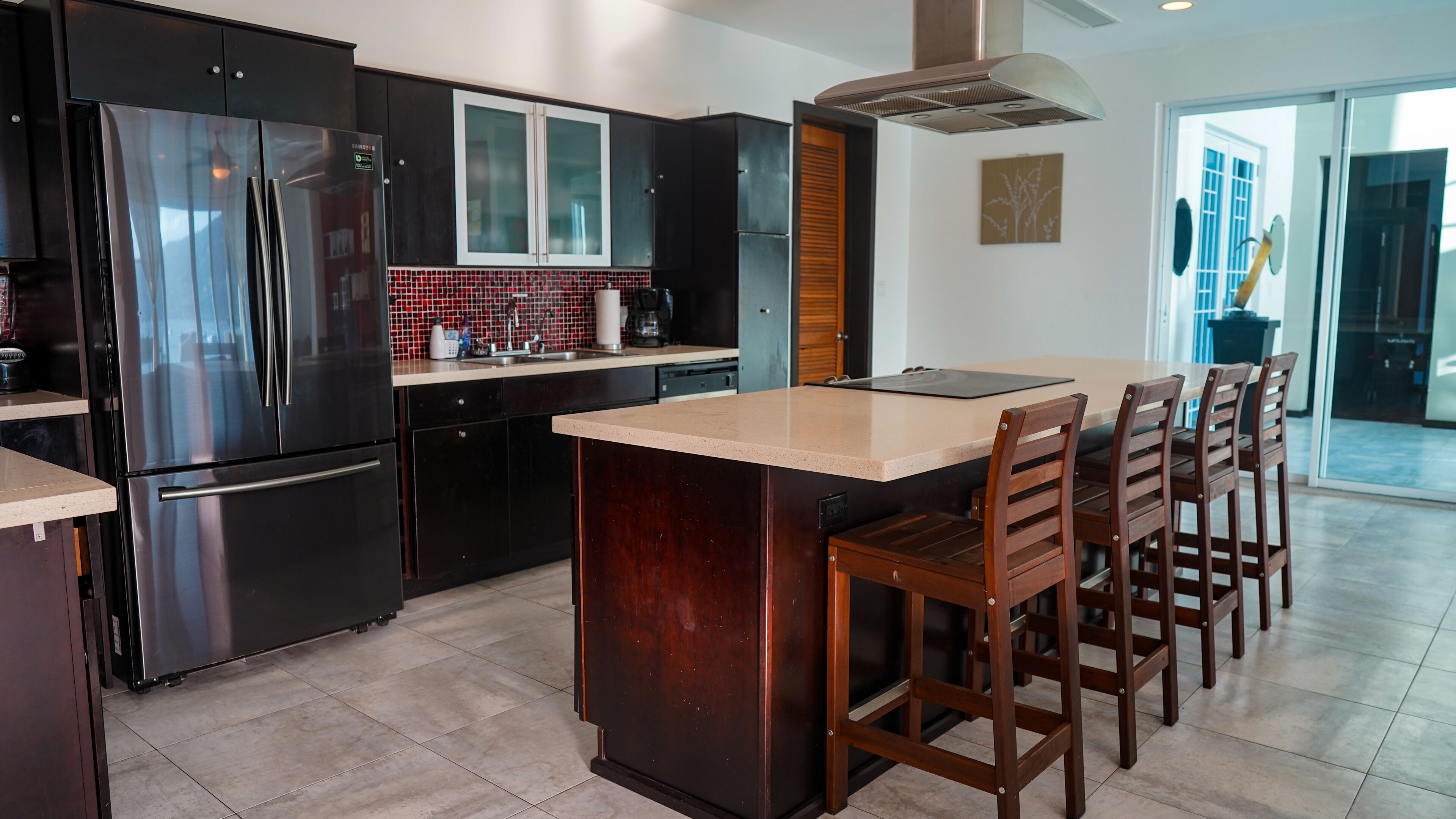 A modern kitchen with a central island, stainless steel appliances, dark cabinetry, and a large window.