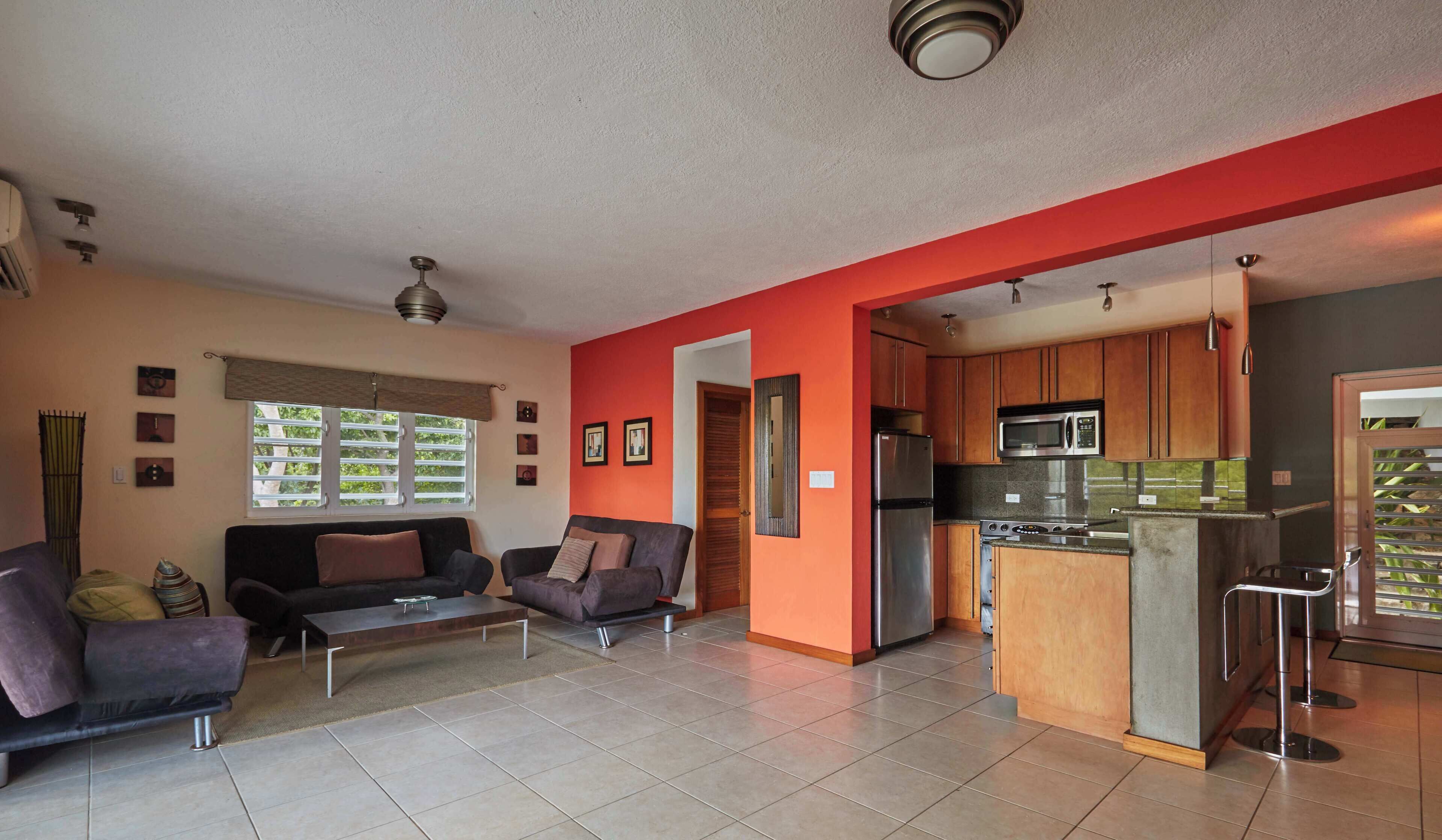 A compact living space with a kitchenette, two sofas, a coffee table, and a dining area with bar stools.