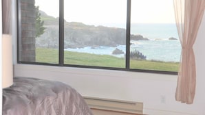 A room with a large window overlooking a rocky coastline and ocean.