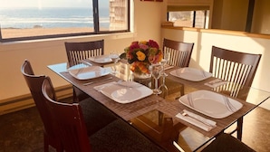 A dining table set for four with a view of the ocean, wooden chairs, and a vase of flowers.