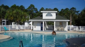 A swimming pool with a white building in the background, surrounded by a white fence and palm trees.
