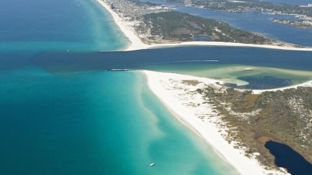 An aerial view of a coastal area with a long stretch of beach, clear blue waters, and a mix of sandy and rocky terrain.