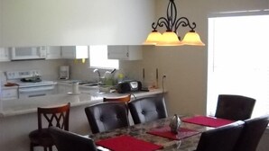 A kitchen with white cabinets, a stove, and a microwave. There is a dining area with a table, chairs, and a chandelier.