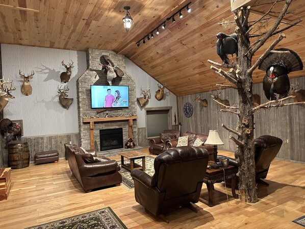 A cozy living room with a fireplace, leather furniture, and various animal mounts on the walls.