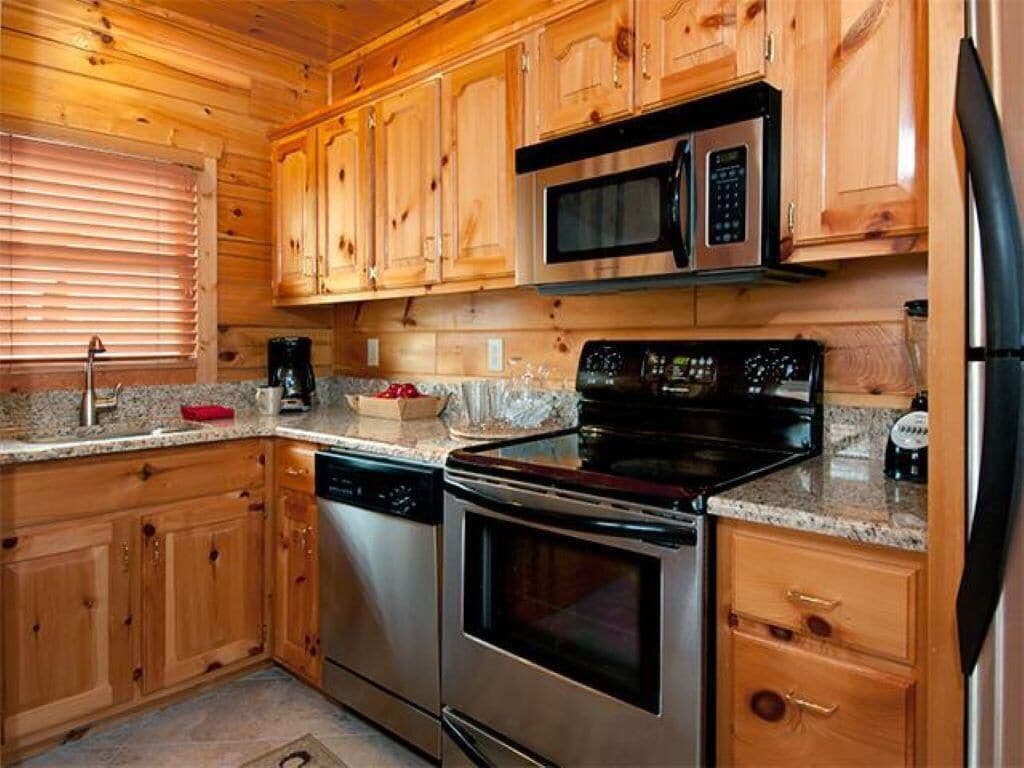 Une cuisine dotée de meubles en bois, d’appareils électroménagers en acier inoxydable, de plans de travail en granit et d’une fenêtre avec des stores.