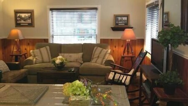 A living room with a sofa, armchairs, a coffee table, and lamps. There are two windows with blinds, a fireplace, and framed pictures on the walls. - Near the Slopes - Big Bear Mountain getaway (Big Bear City)