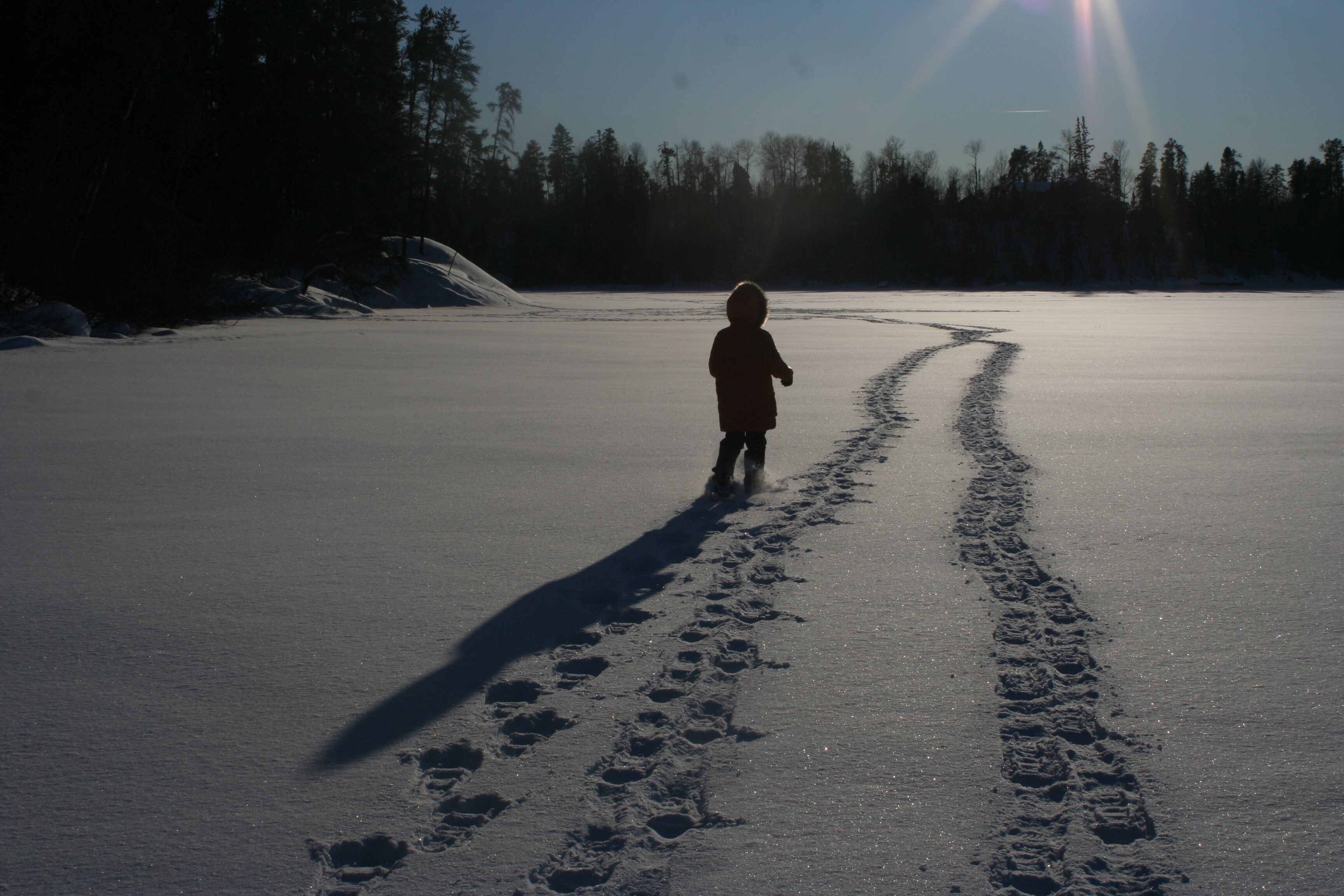 Un niño caminando por un sendero cubierto de nieve, con huellas que se alejan de la cámara.