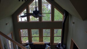 En rymlig loftvåning med högt i tak, stora fönster med utsikt över omgivningarna, en soffa i läder med kuddar och en öppen spis.
