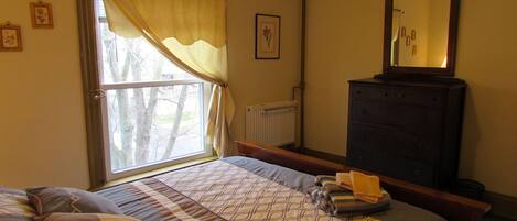 Una camera da letto con un letto, una cassettiera, una finestra con tende e un termosifone.