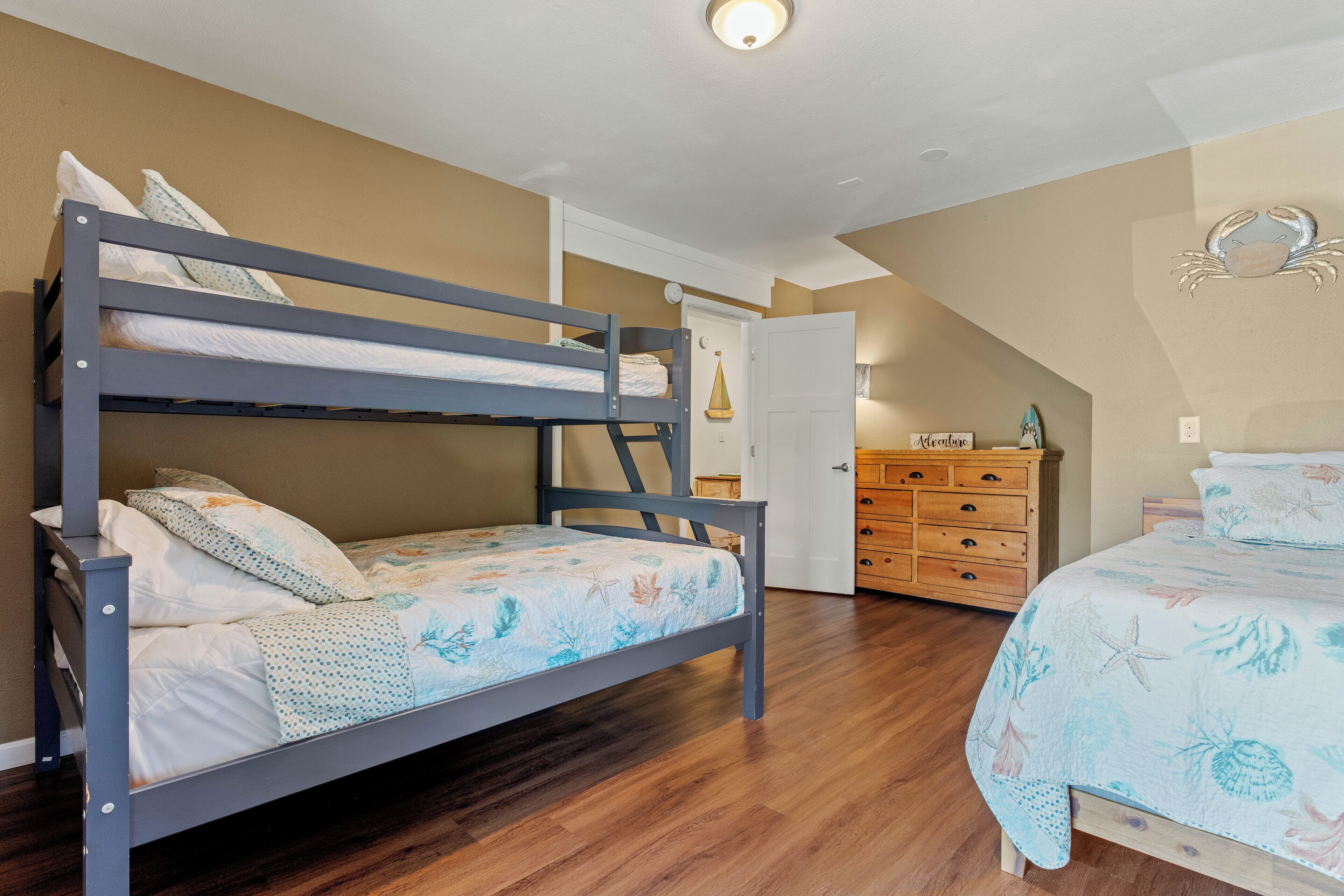 Un lit superposé avec une couvre-lit à motifs floraux, une commode en bois et une porte décorée de motifs représentant la lune et les étoiles.