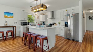 Eine moderne Küche mit weißen Schränken, einem Edelstahlkühlschrank, Holzbarhocker und einer großen Kochinsel.