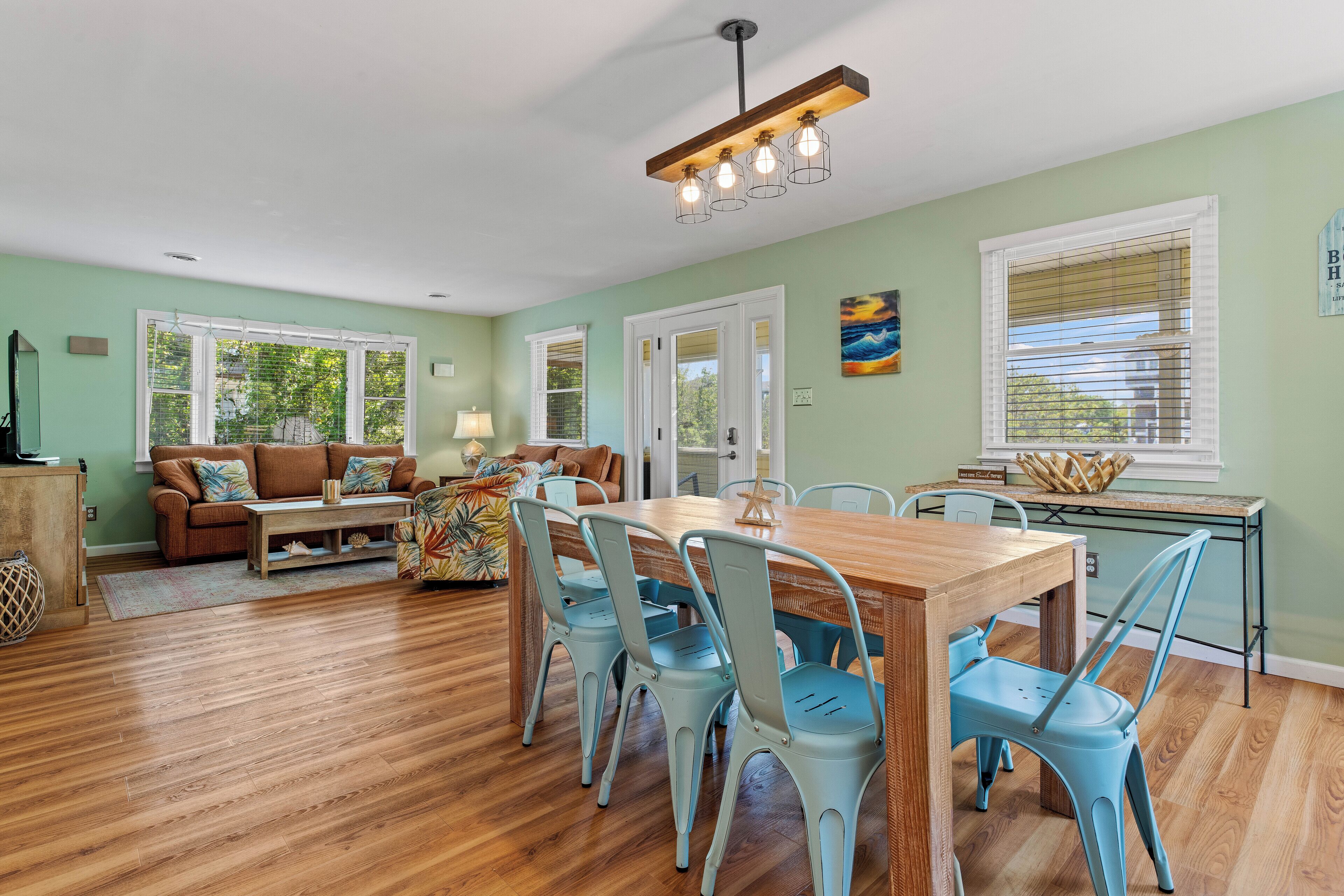 A spacious living room with a wooden dining table, blue chairs, and a sofa set.