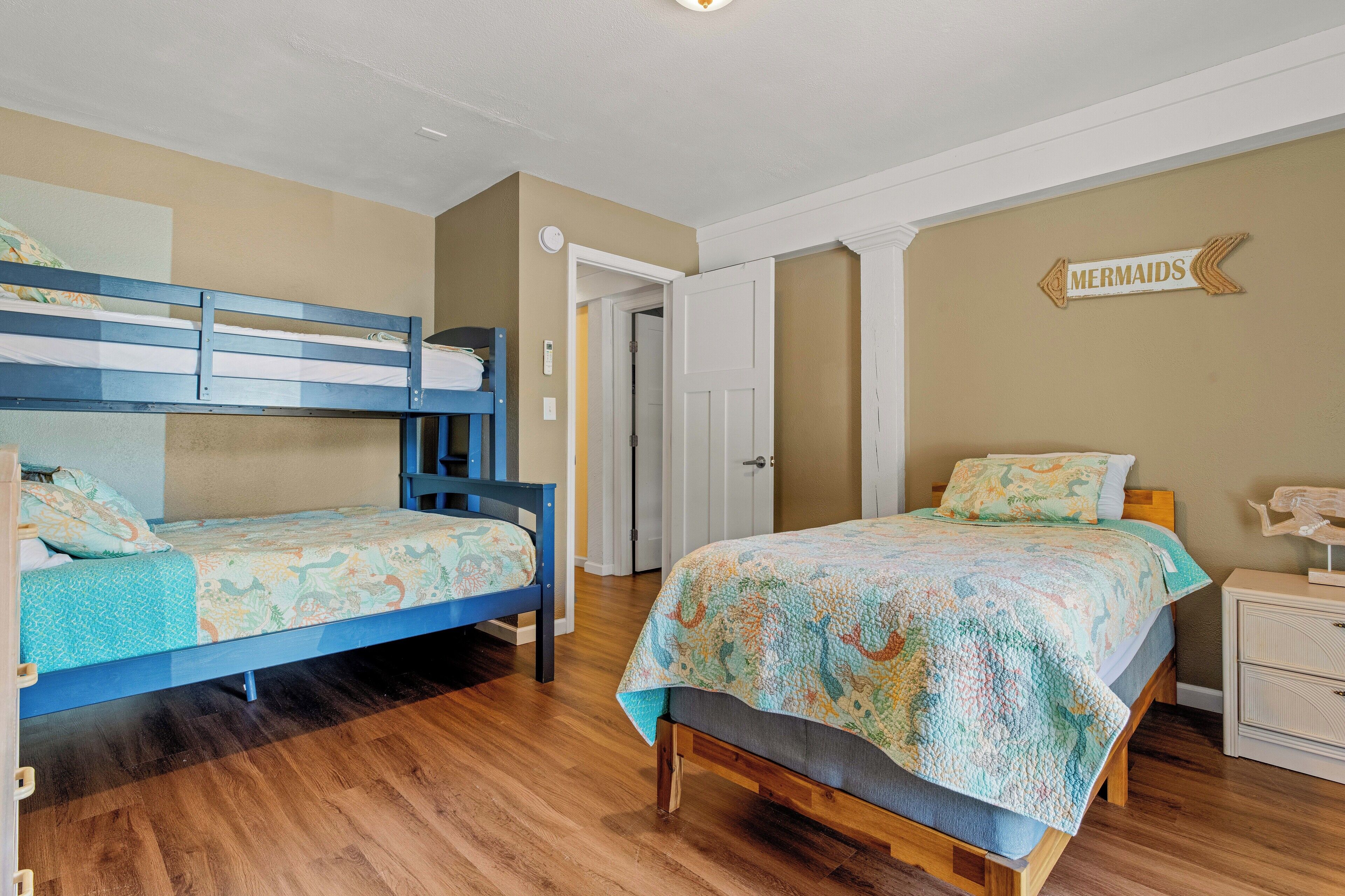 A bedroom with two bunk beds, a wooden floor, a door, and a wall sign that says "MERMAIDS".