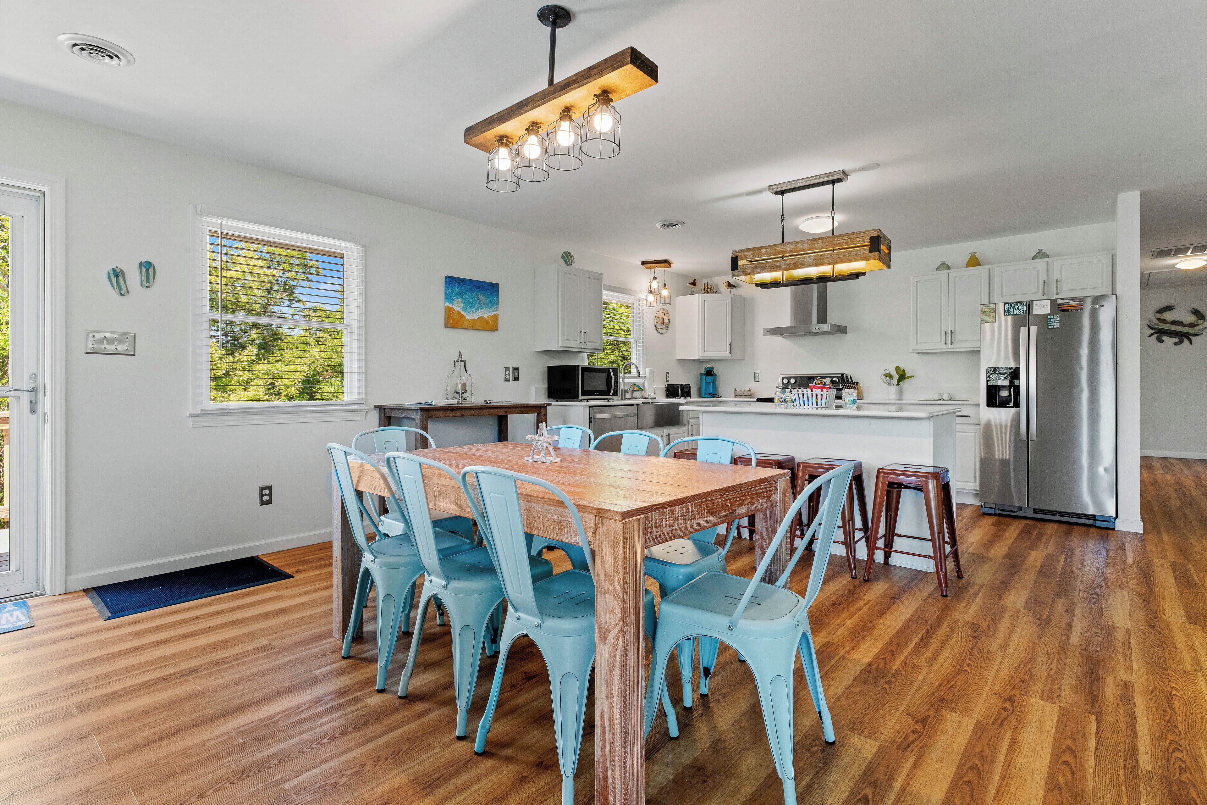 A modern kitchen with a wooden dining table, light blue chairs, stainless steel appliances, and a view of the outdoors.