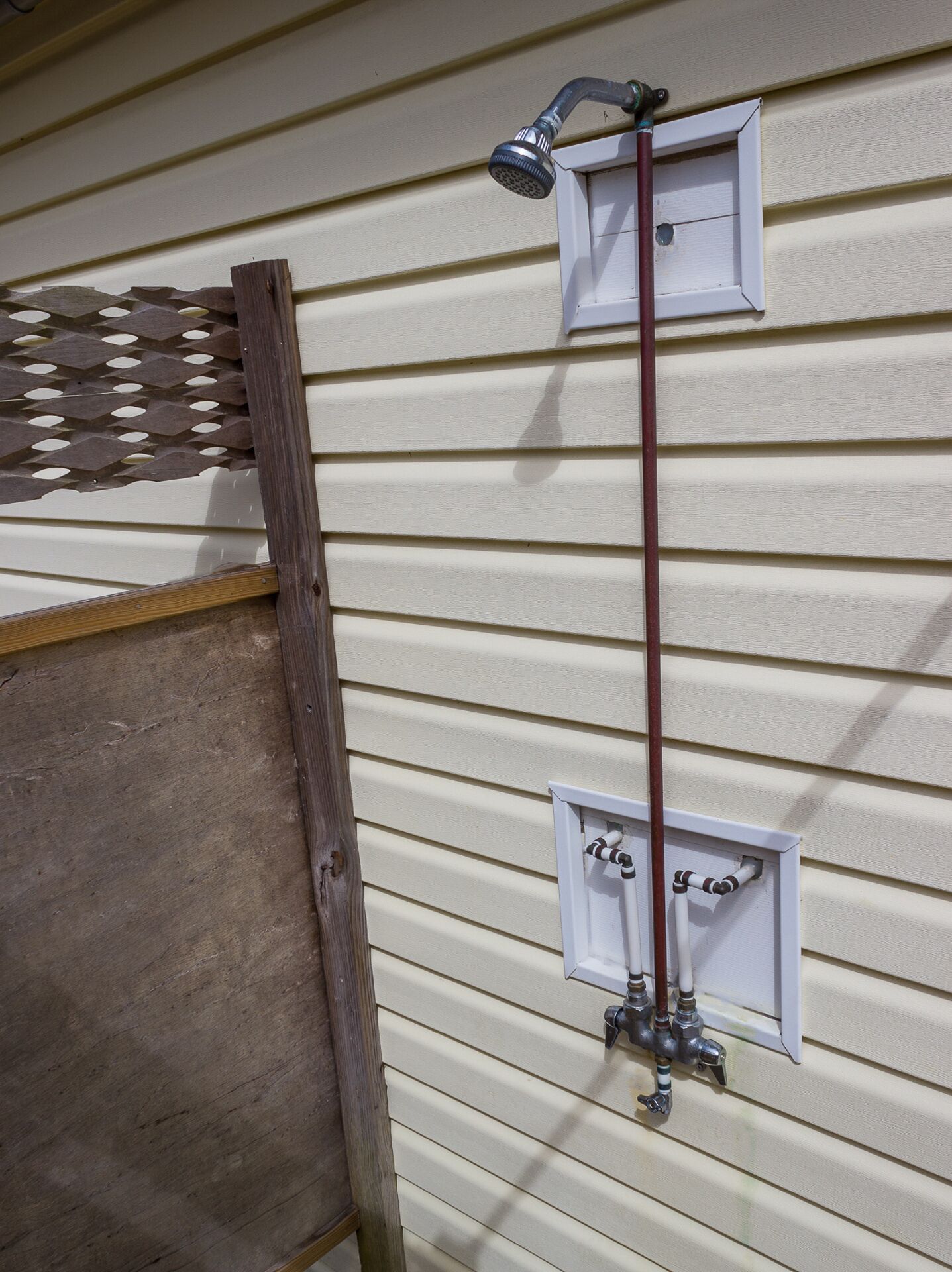 A wooden deck attached to a house with a metal shower head and pipes.
