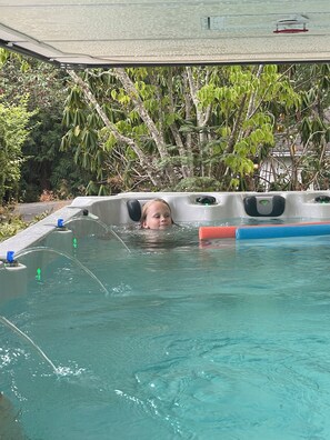 A person in a hot tub with a view of a building and trees in the background.