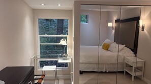 A bedroom with a bed, bedside table, lamp, and a window with a view of trees. - The Escape - Private Luxury House in the Trees - Swim Spa. Pet Friendly! (Cobble Hill)