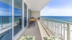 Un balcon avec une table et des chaises, donnant sur une plage parsemée de parasols.