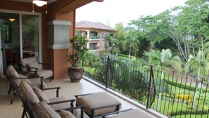 A balcony with outdoor furniture and a view of a landscaped garden and a building in the background. - Luxury Oceanfront Los Suenos Condo overlooking Herradura Bay (Los Suenos)