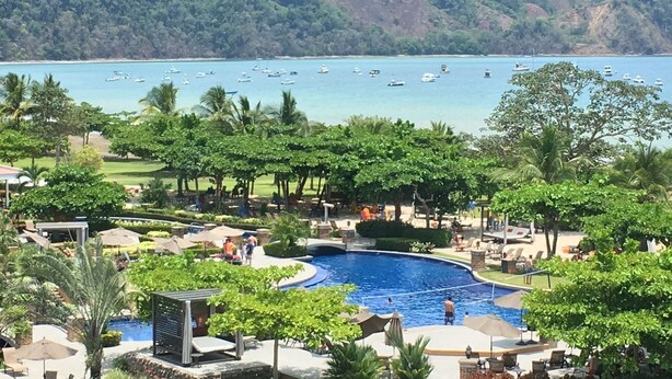 A resort with a swimming pool, lounge areas, and a view of the sea with boats. - Luxury Oceanfront Los Suenos Condo overlooking Herradura Bay (Los Suenos)