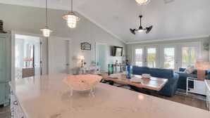 A spacious kitchen with a large island, pendant lighting, and a cozy seating area with a blue sofa. - 🌴Buckeye🌴Steps to Sand | Sleeps 8 w/ Gulf Views + Outdoor Shower (Navarre)
