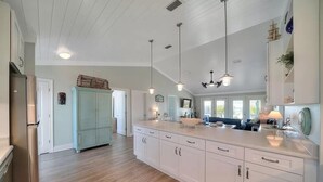 A spacious kitchen with white cabinetry, a central island, pendant lighting, and a view to the living area. - 🌴Buckeye🌴Steps to Sand | Sleeps 8 w/ Gulf Views + Outdoor Shower (Navarre)