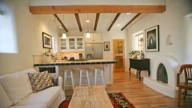 A living room with a sofa, a wooden coffee table, and a kitchen area with a bar stool.