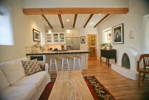 A living room with a sofa, a wooden coffee table, and a kitchen area with a bar stool.