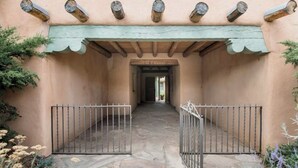 A stone-paved entrance with a metal gate, a covered walkway with wooden beams, and a building facade with a scalloped cornice.