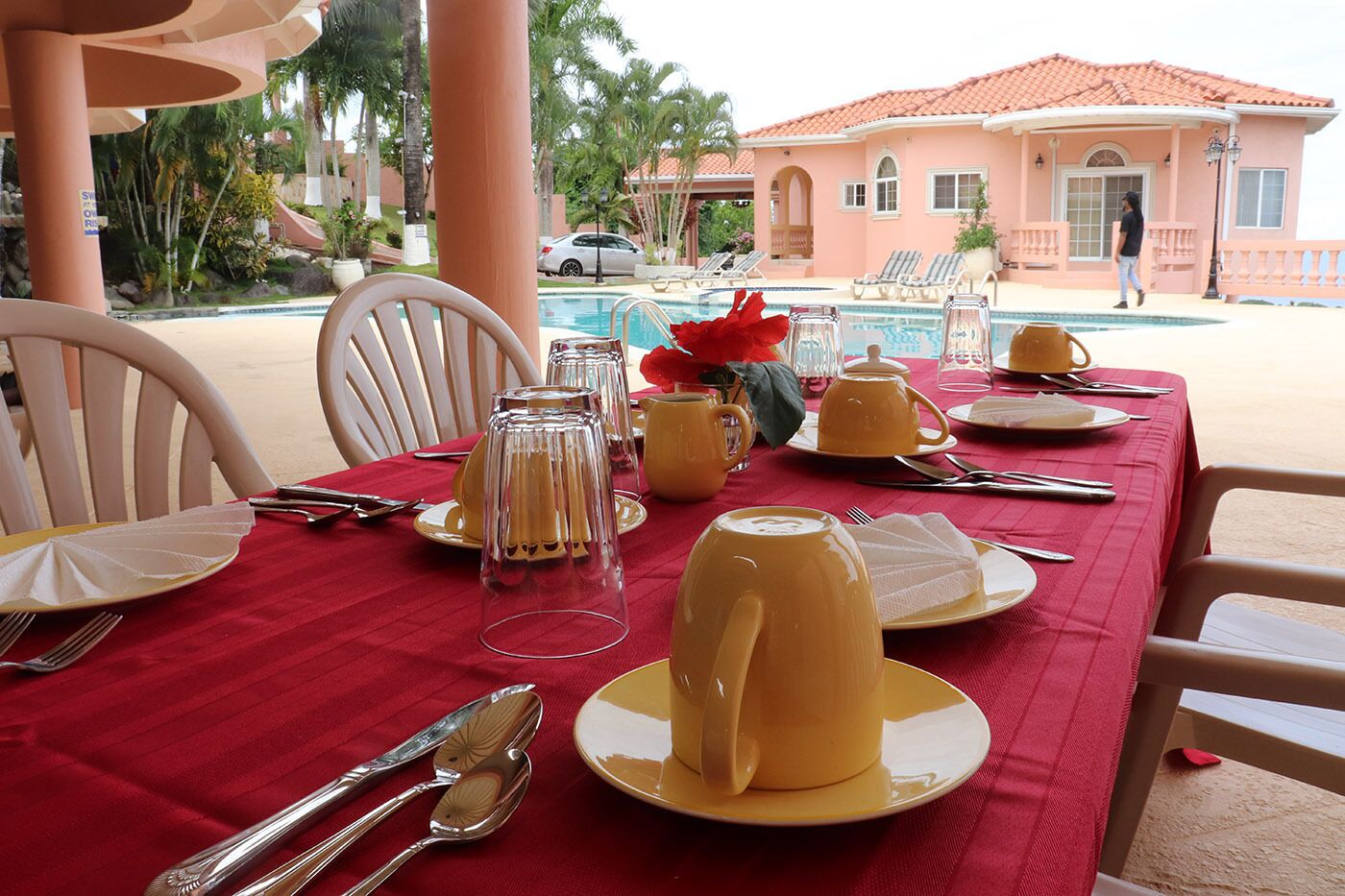 A dining table set with yellow plates, clear glassware, and a red tablecloth.